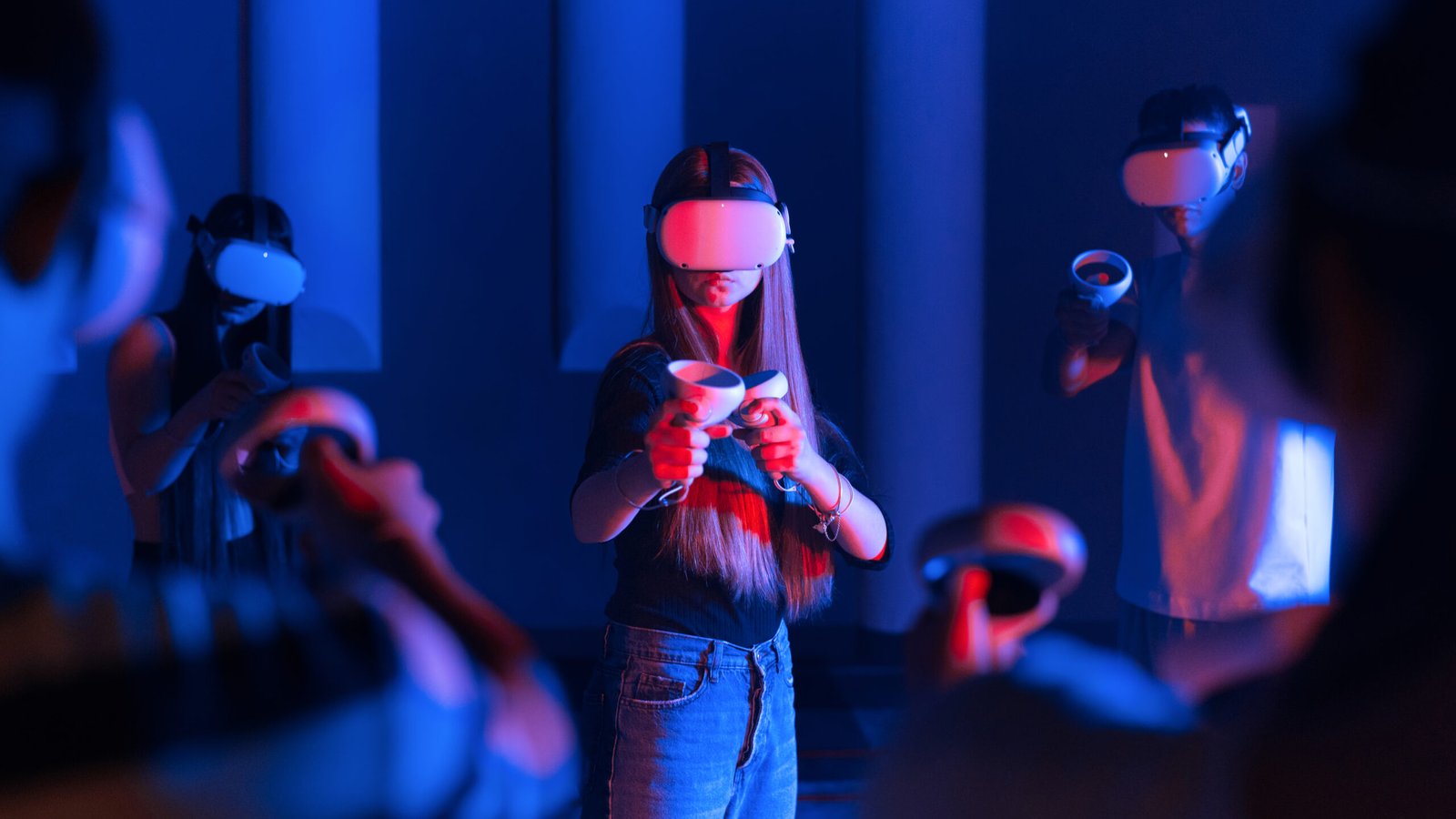 A team of young friends using virtual reality VR equipment on an arena. A girl in the center and other playmates in the background. Neon lights